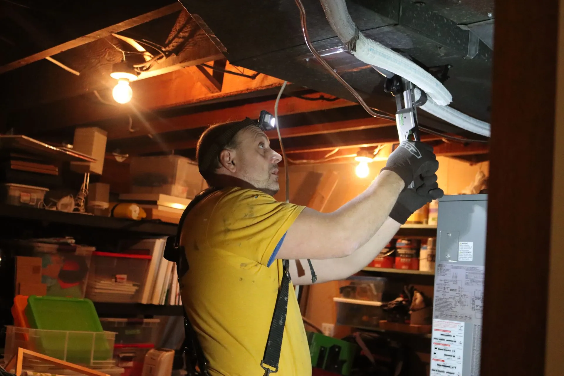 Technician wearing a headlamp working on ceiling pipes and ductwork in a basement.