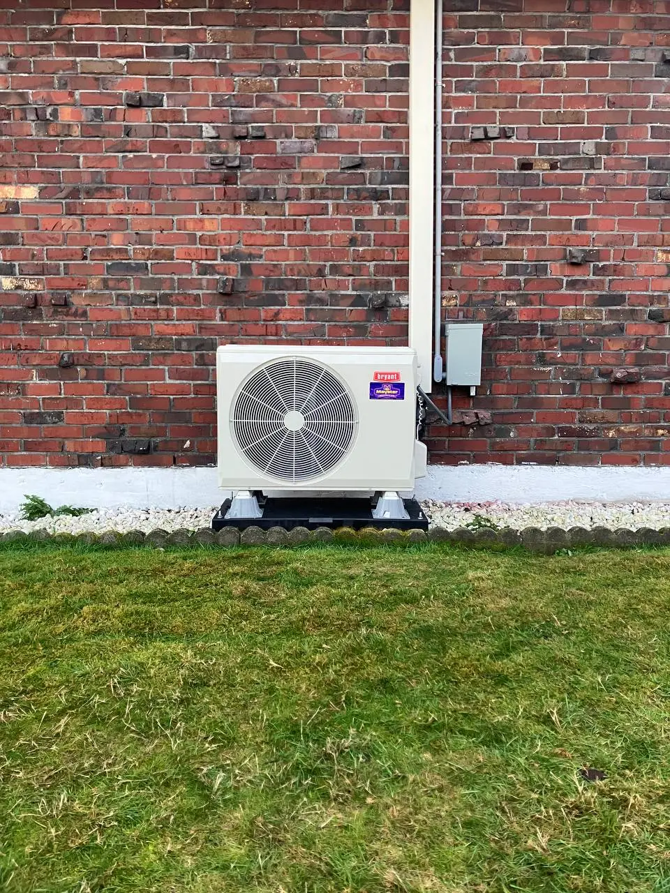 A compact HVAC condenser sits neatly against a red brick wall thanks to Heat Pump Services Greater Puget Sound.
