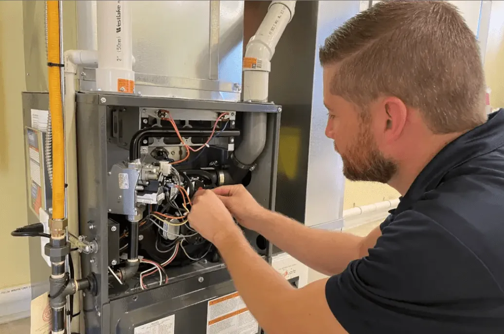 Technician adjusting electrical wiring inside an open HVAC furnace system during maintenance.
