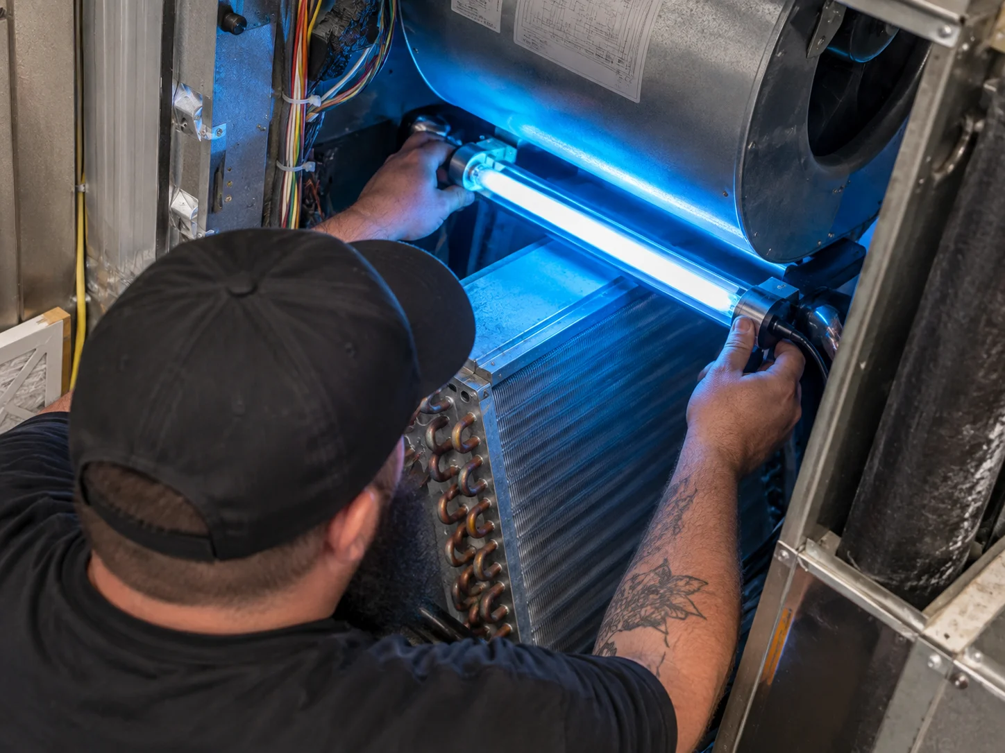 A technician installing a glowing blue germicidal lamp inside an HVAC unit during professional UV Light Services.