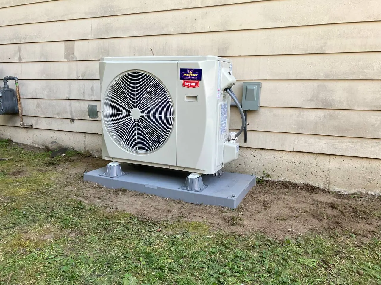 Outdoor Bryant heat pump unit installed on a pad along beige siding by expert Heating System Services Greater Puget Sound.