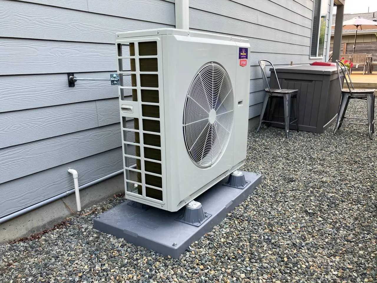 A modern outdoor heat pump condenser unit installed on a pad outside a house by Heat Pump Services Greater Puget Sound.