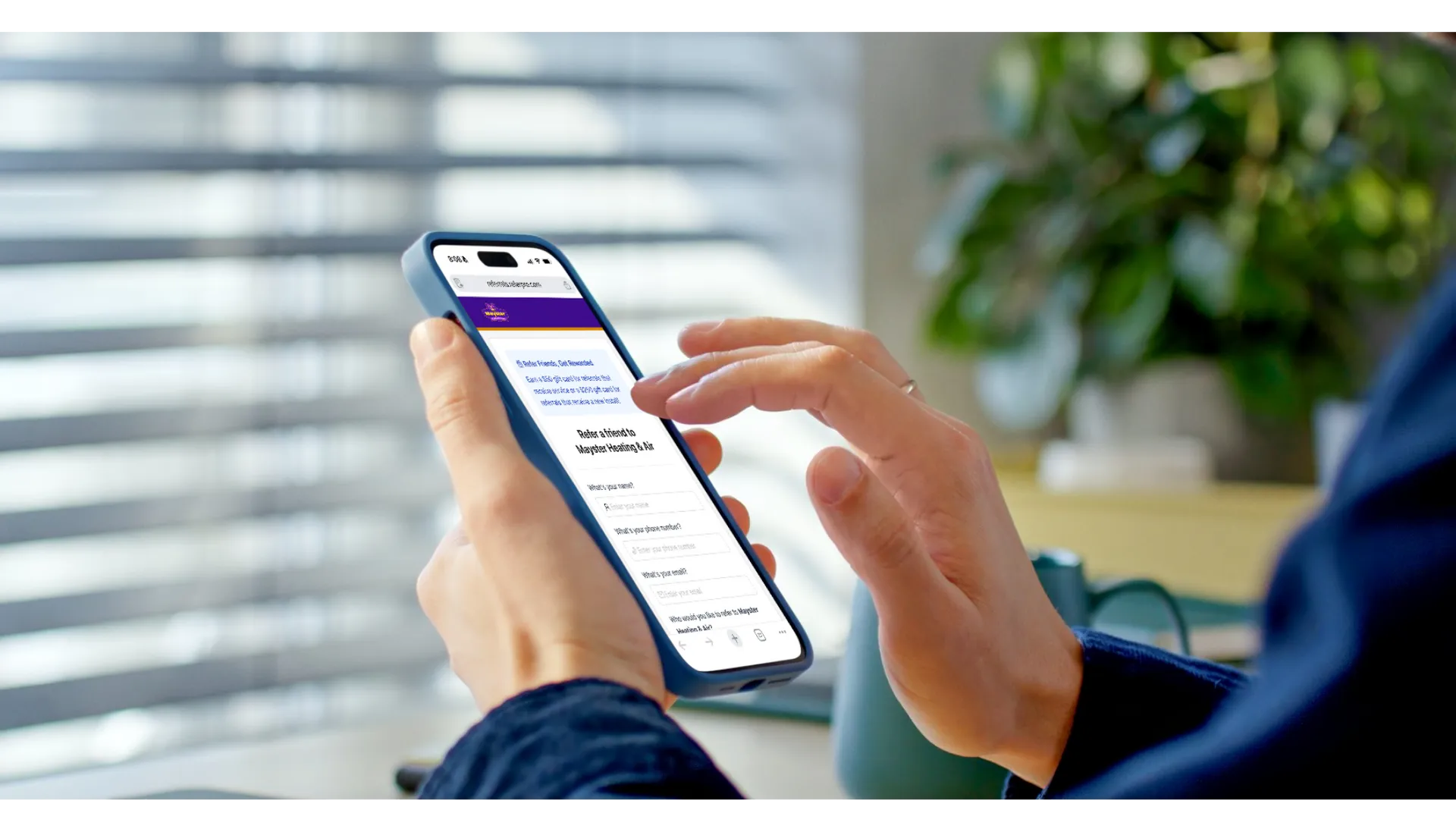 Hands holding a blue smartphone displaying a referral program form for Mayster Heating and Air.