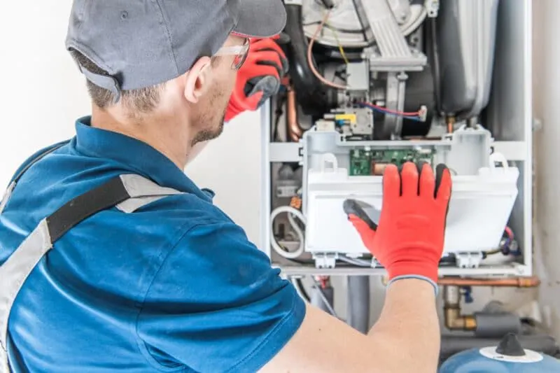 Technician in blue uniform and red gloves inspecting open wall mounted heating boiler system.