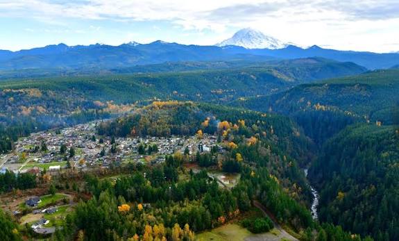 Aerial view of Carbonado above a forested river gorge with Mount Rainier behind, where Mayster provides HVAC services in Carbonado WA for local homes