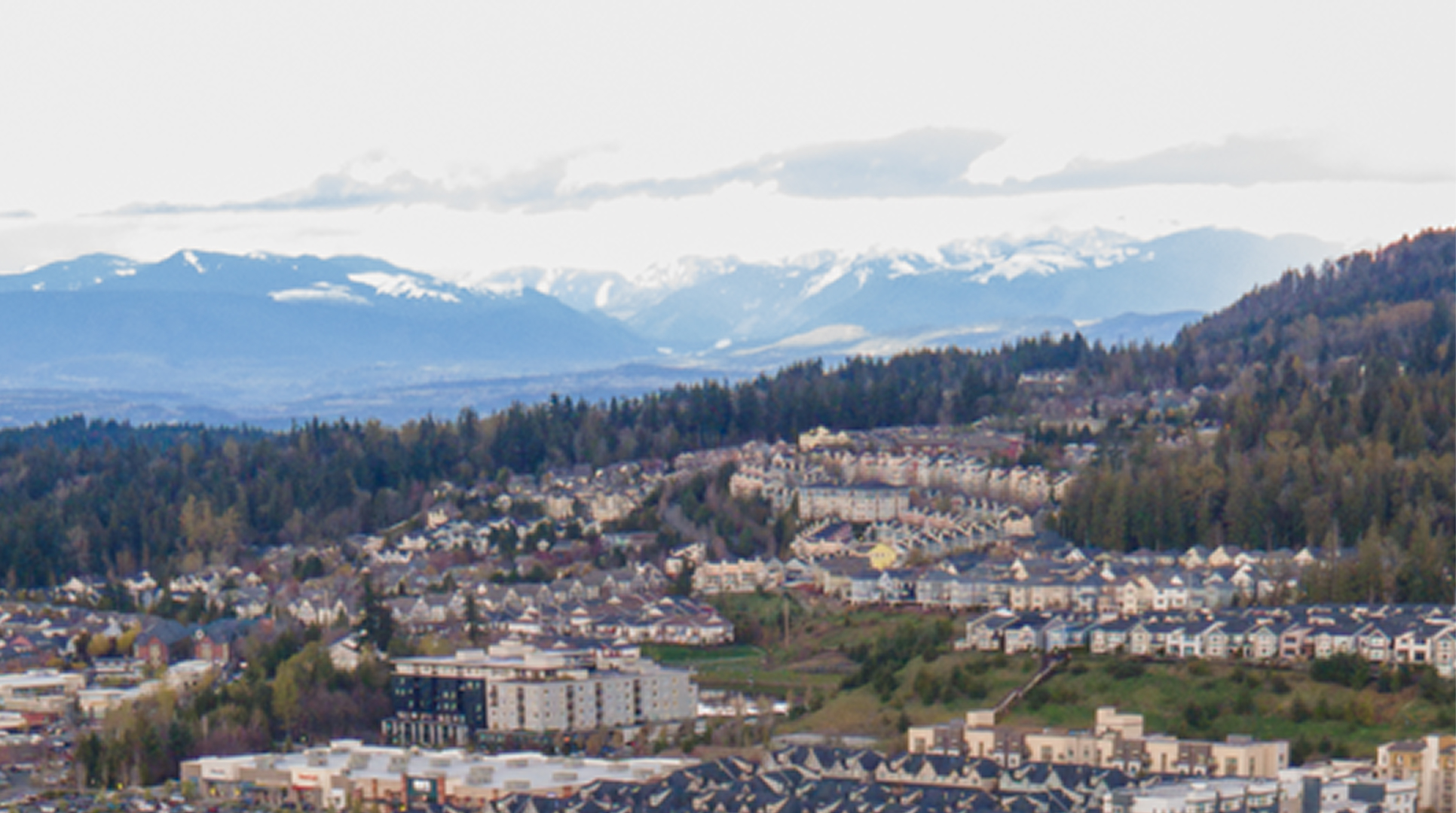 Hillside neighborhoods of Issaquah with forested slopes and snowy Cascade peaks behind, where Mayster delivers HVAC services in Issaquah WA to area homeowners